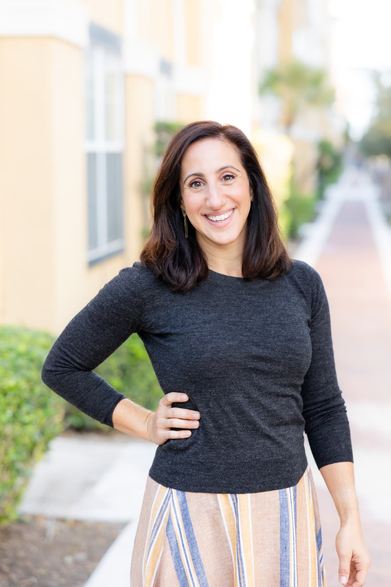 Victoria Planells smiling, wearing a charcoal sweater, standing on a sunny street